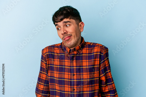 Young mixed race man isolated on blue background shrugs shoulders and open eyes confused.