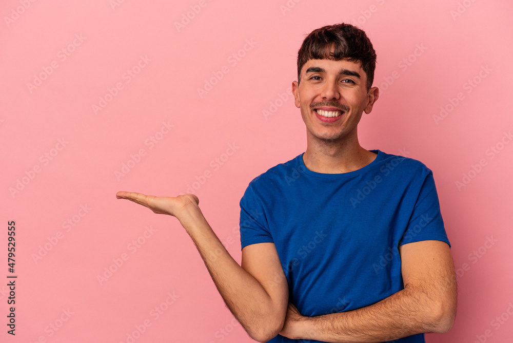 Young mixed race man isolated on pink background showing a copy space on a palm and holding another hand on waist. Young mixed race man isolated on pink background showing a copy space on a palm and holding another hand on waist.