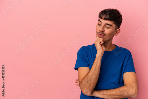 Young mixed race man isolated on pink background looking sideways with doubtful and skeptical expression.