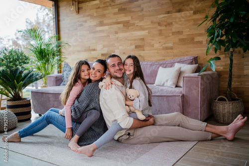 Two happy sisters with mother and father sitting on floor hugging and looking at camera at home