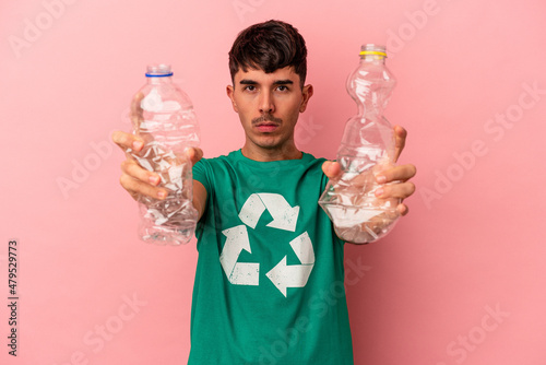 Young mixed race man recycled plastic isolated on pink background