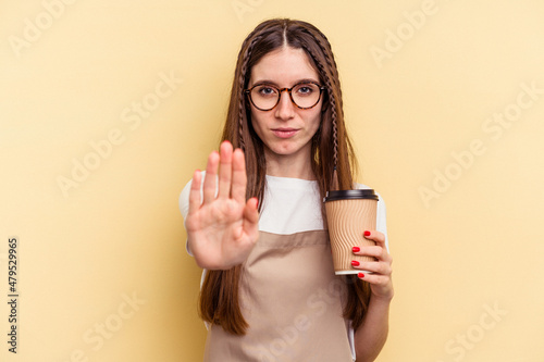 Restaurant waiter woman holding a take away coffee isolated on yellow background standing with outstretched hand showing stop sign  preventing you.