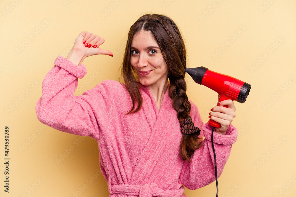 Young woman holding a hairdryer isolated on yellow background feels proud and self confident, example to follow. Young woman holding a hairdryer isolated on yellow background feels proud and self confident, example to follow.