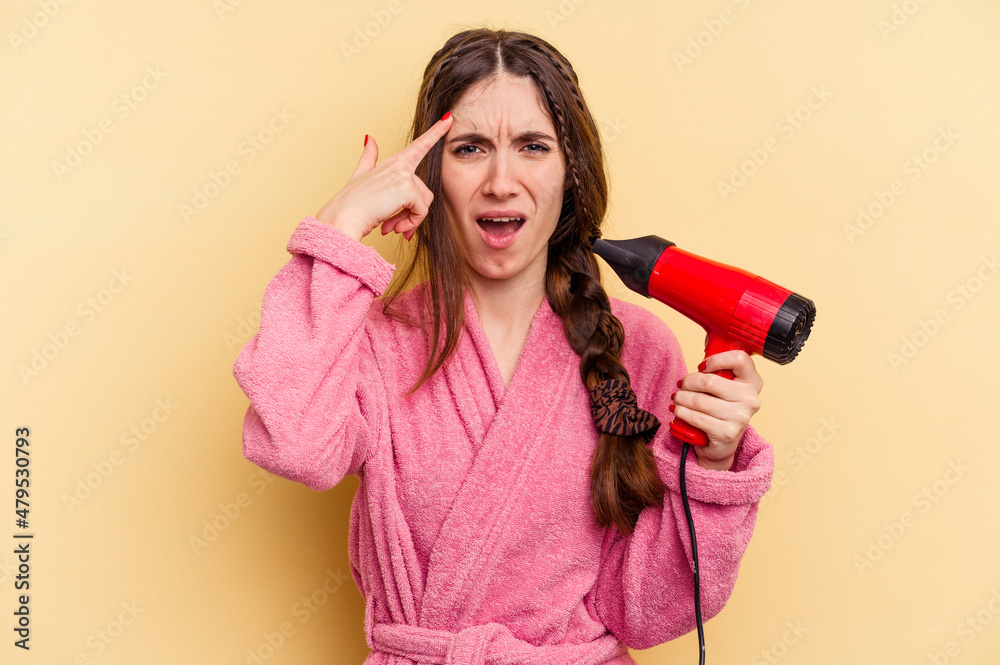 Young woman holding a hairdryer isolated on yellow background showing a disappointment gesture with forefinger. Young woman holding a hairdryer isolated on yellow background showing a disappointment gesture with forefinger.