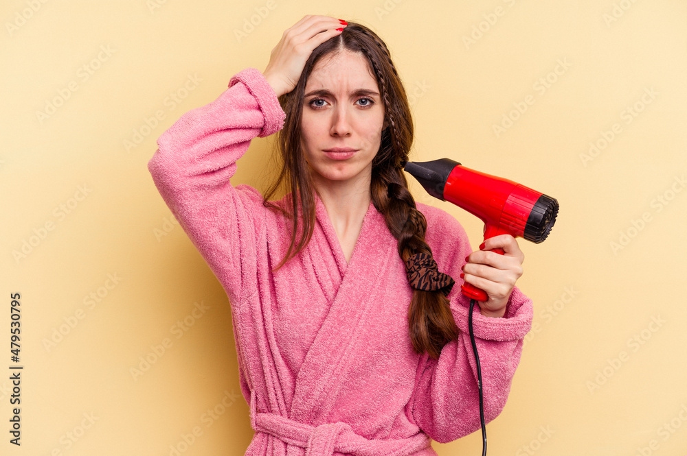 Young woman holding a hairdryer isolated on yellow background being shocked, she has remembered important meeting. Young woman holding a hairdryer isolated on yellow background being shocked, she has remembered important meeting.