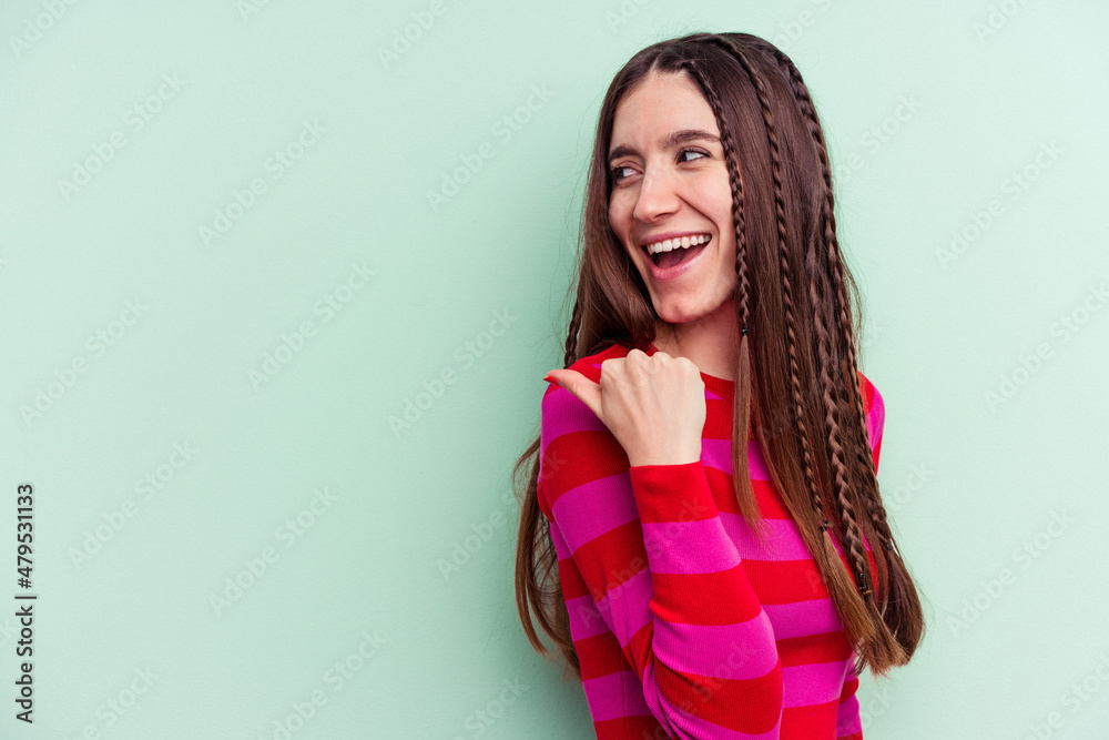 Young caucasian woman isolated on green background points with thumb finger away, laughing and carefree. Young caucasian woman isolated on green background points with thumb finger away, laughing and carefree.