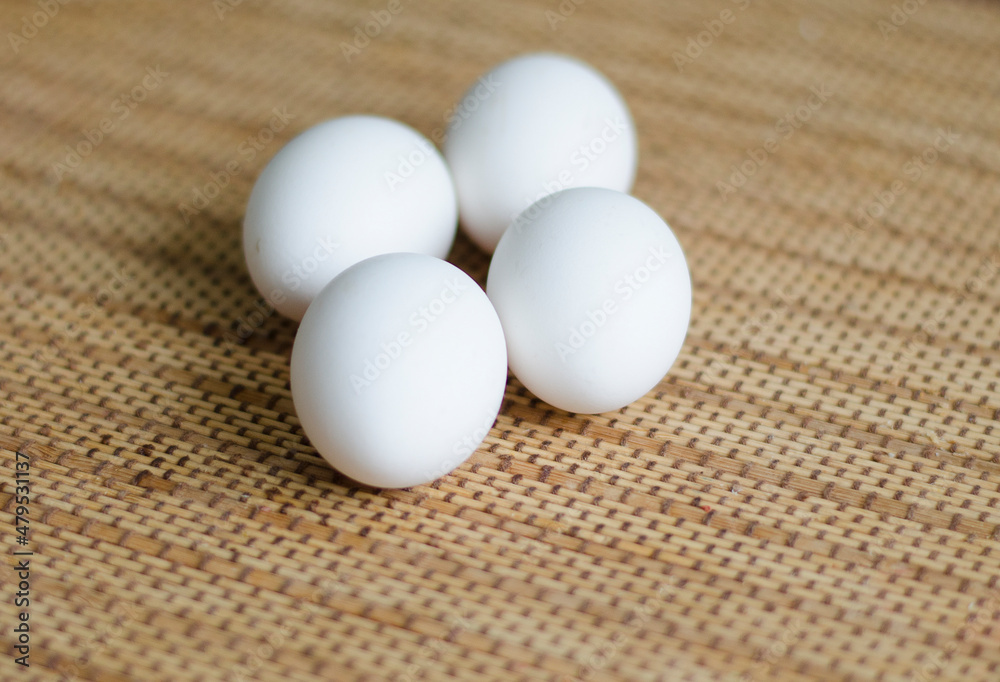 Four white chicken eggs lie on a bamboo mat, close-up Four white chicken eggs lie on a bamboo mat, close-up