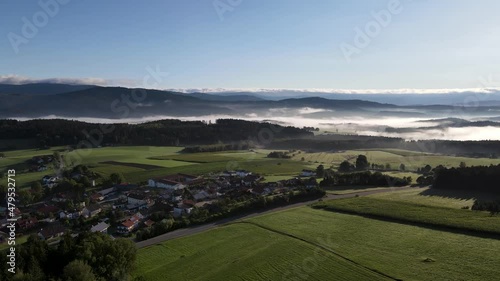 Drone flight over a small village at sunrise in Bavaria, Germany. Mountains along the place and fog in the background photo