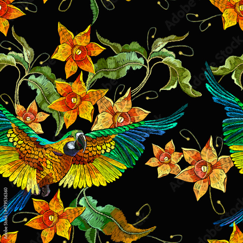 Yellow narcissuses and fying parrot, seamless pattern. Embroidery. Template for clothes, textiles, t-shirt design. Beautiful tropiacal birds on black background. Botanical vector illustration photo