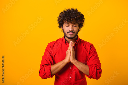 Peaceful mind, harmony. Portrait of man holding hands cupped and praying with grateful expression, practicing yoga meditation. Indoor studio shot isolated on orange background photo