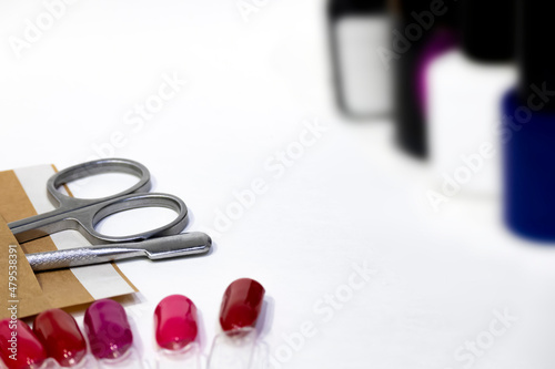 Manicure, pedicure background with professional metal sterile cuticle removal tools. Pusher, nail scissors, samples red nail polish, blurred silhouettes of bottles with gel varnishes with copy space. photo