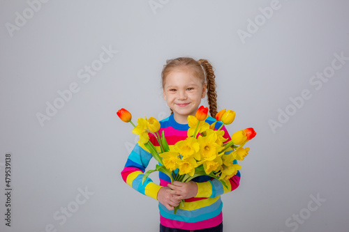 a cute little girl in a multicolored sweater holds a bouquet of spring flowers on a white background