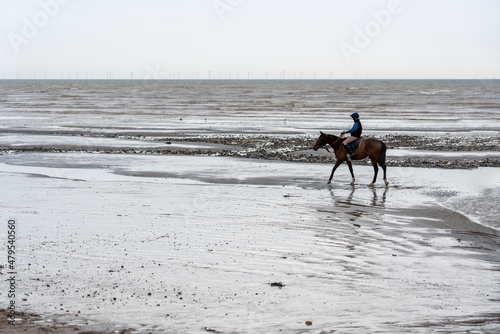 FERRING BEACH, WEST SUSSEX, UK - CIRCA 2021 JANUARY: A horserider riding a brown horse on a wet sandy beach by the sea on a cloudy day.
