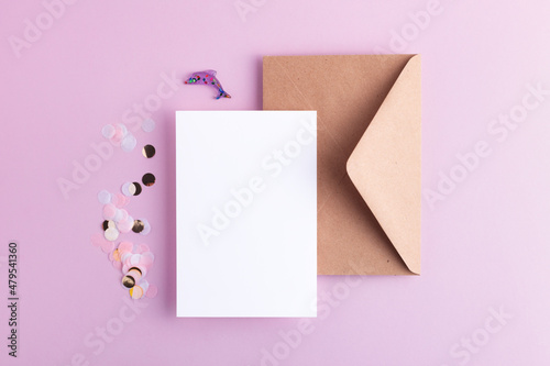 Empty card with confetti, envelope and decorative lavender dolphin on pastel lilac background. Flat lay with blank space for your design. 