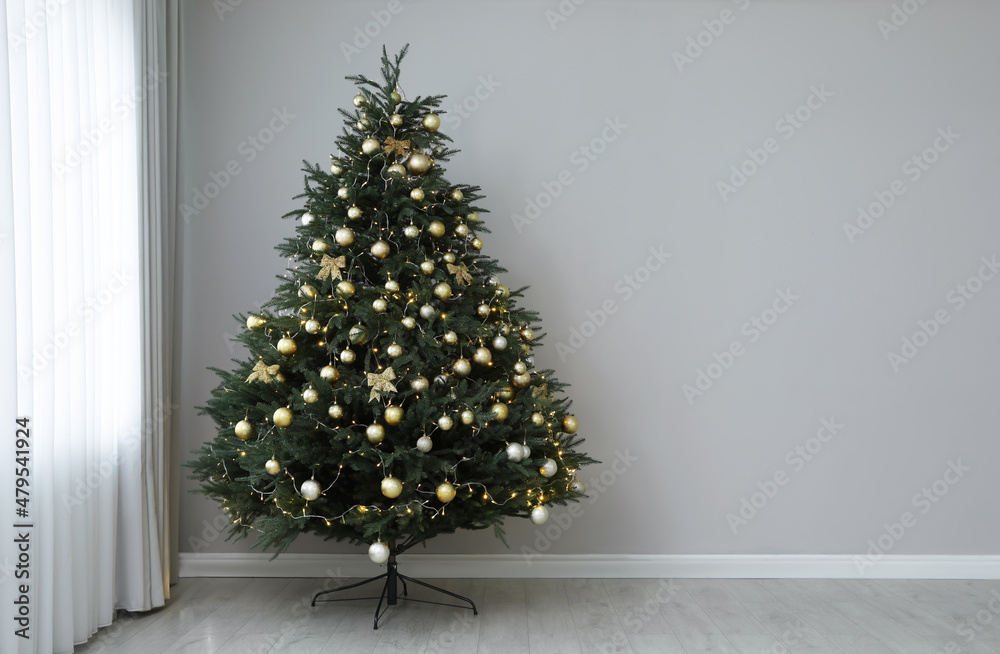 Beautifully decorated Christmas tree near grey wall indoors, space for text фотография Stock