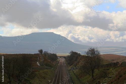 Settle to Carlisle Railway passes over Blea Moor on Whernside with the looming mass of Ingleborough Fell in the distance. photo