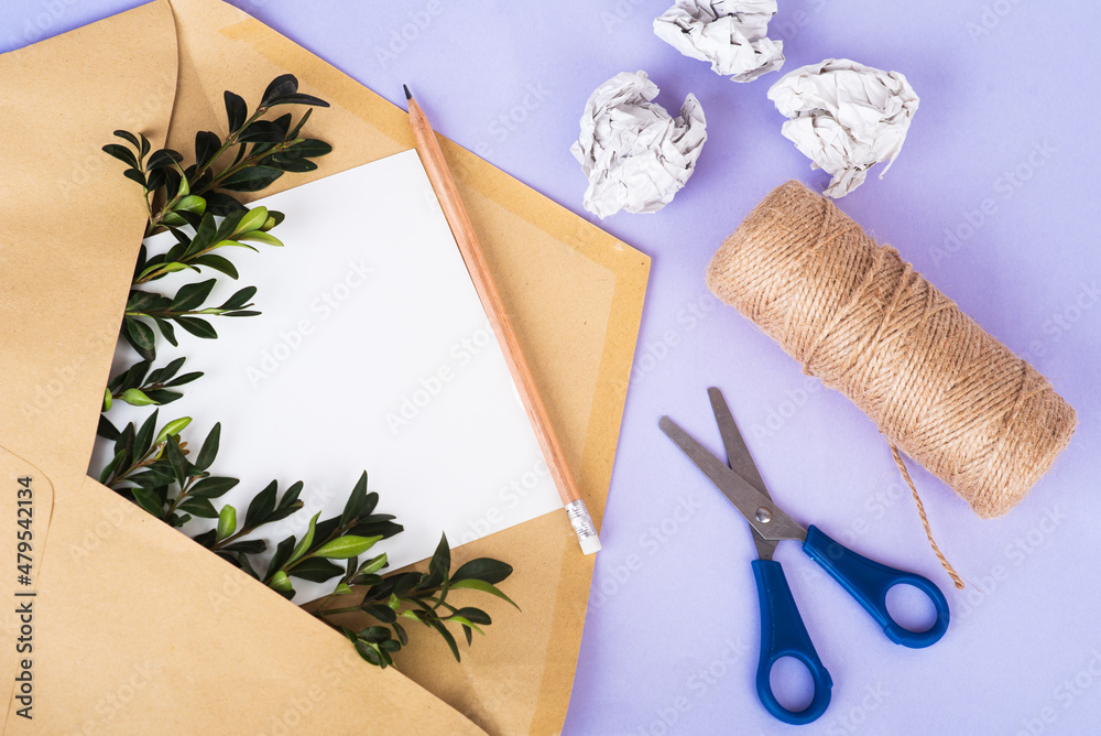 Craft paper envelope with empty paper and green twigs among crumpled paper and bundle winding on Very Peri background Craft paper envelope with empty paper and green twigs among crumpled paper and bundle winding on Very Peri background
