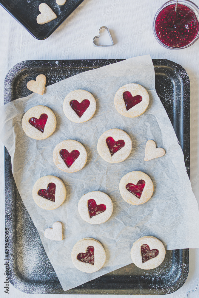 Portrait flat lay image of hear shaped Linzer jam and jelly filled cookies. Baked treats concept including jam, cookie cutters, icing sugar and baking sheets. Romance and love food concept. Portrait flat lay image of hear shaped Linzer jam and jelly filled cookies. Baked treats concept including jam, cookie cutters, icing sugar and baking sheets. Romance and love food concept.