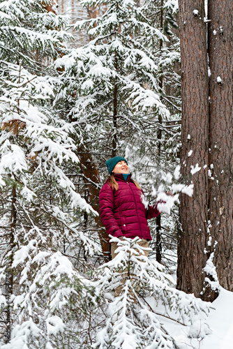 Young cheerful woman in red jacket enjoying snow falling from fir tree in winter forest, walking beauty in nature, active lifestyle winter hiking © Lena_viridis