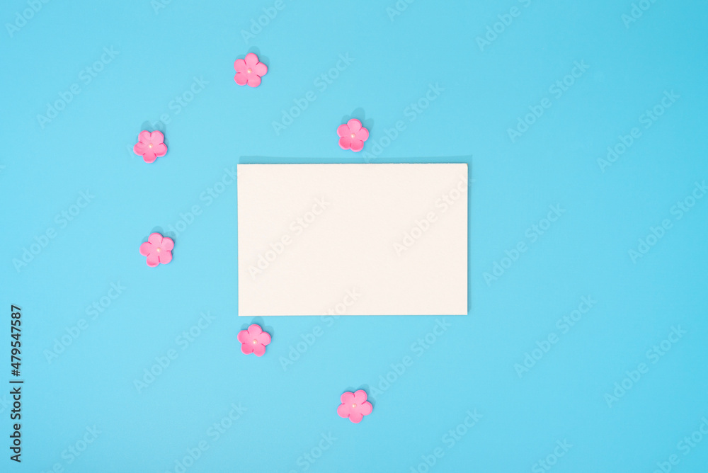 White paper card note with small pink flowers on blue background. Greeting card. Love, Valentines Day or other holiday concept. Flat lay style with copy space White paper card note with small pink flowers on blue background. Greeting card. Love, Valentines Day or other holiday concept. Flat lay style with copy space