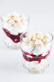 Portion dessert with meringue, coconut cream and cherries in glasses on a light background. Sugar, gluten and lactose free and vegan.