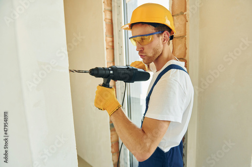 Holding drill. Young man working in uniform at construction at daytime