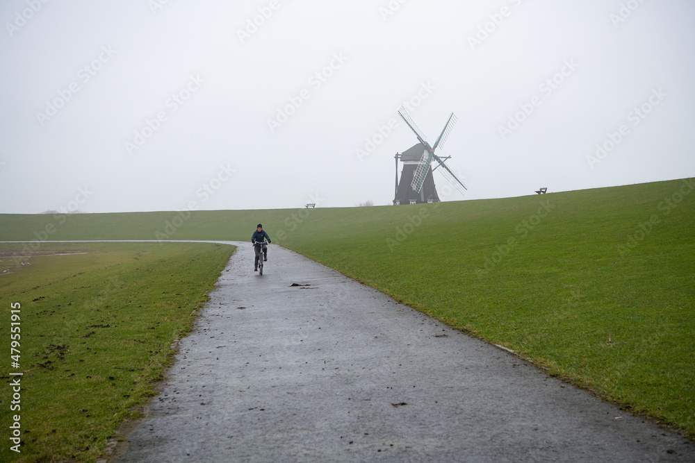 Obraz premium Fahrradtour auf dem Deich. Im Hintergrund die Nordermühle, Insel Pellworm
