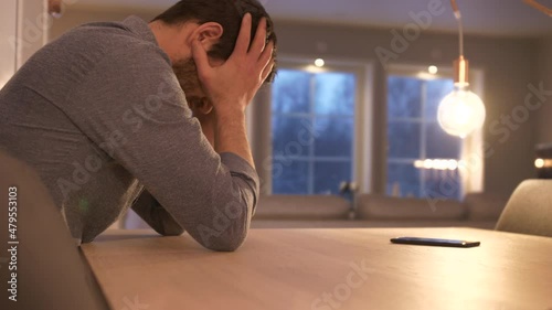Man reads notification and gets upset while sitting near wooden table inside photo