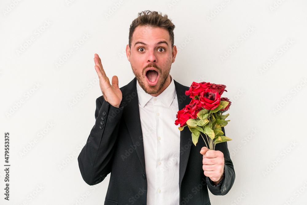 Young caucasian man holding bouquet of flowers isolated on white background surprised and shocked. Young caucasian man holding bouquet of flowers isolated on white background surprised and shocked.
