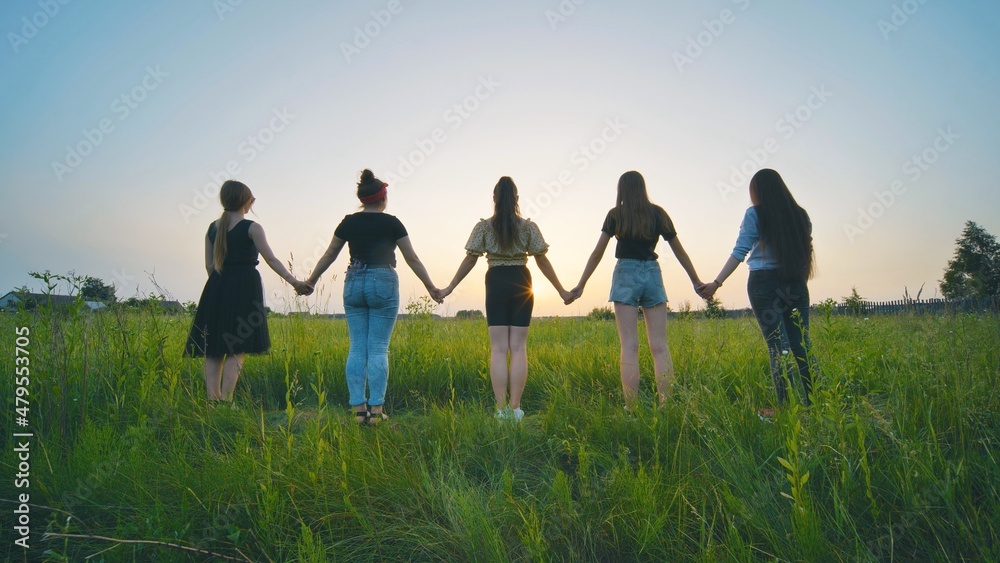 Girls friends go hand in hand at sunset across the field. Girls friends go hand in hand at sunset across the field.