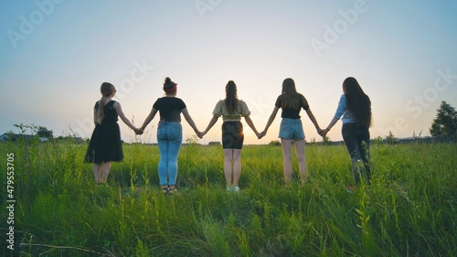 Girls friends go hand in hand at sunset across the field. © Довидович Михаил