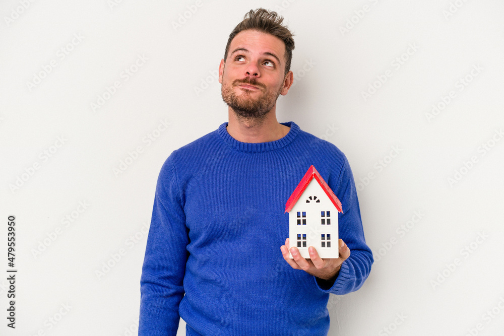 Young caucasian man holding a little house isolated on white background dreaming of achieving goals and purposes Young caucasian man holding a little house isolated on white background dreaming of achieving goals and purposes