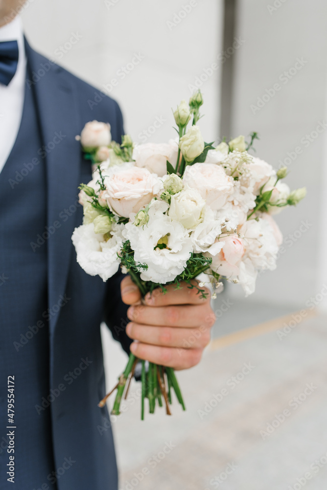 The groom in a blue suit holds in his hand a delicate wedding bouquet for his beloved bride The groom in a blue suit holds in his hand a delicate wedding bouquet for his beloved bride