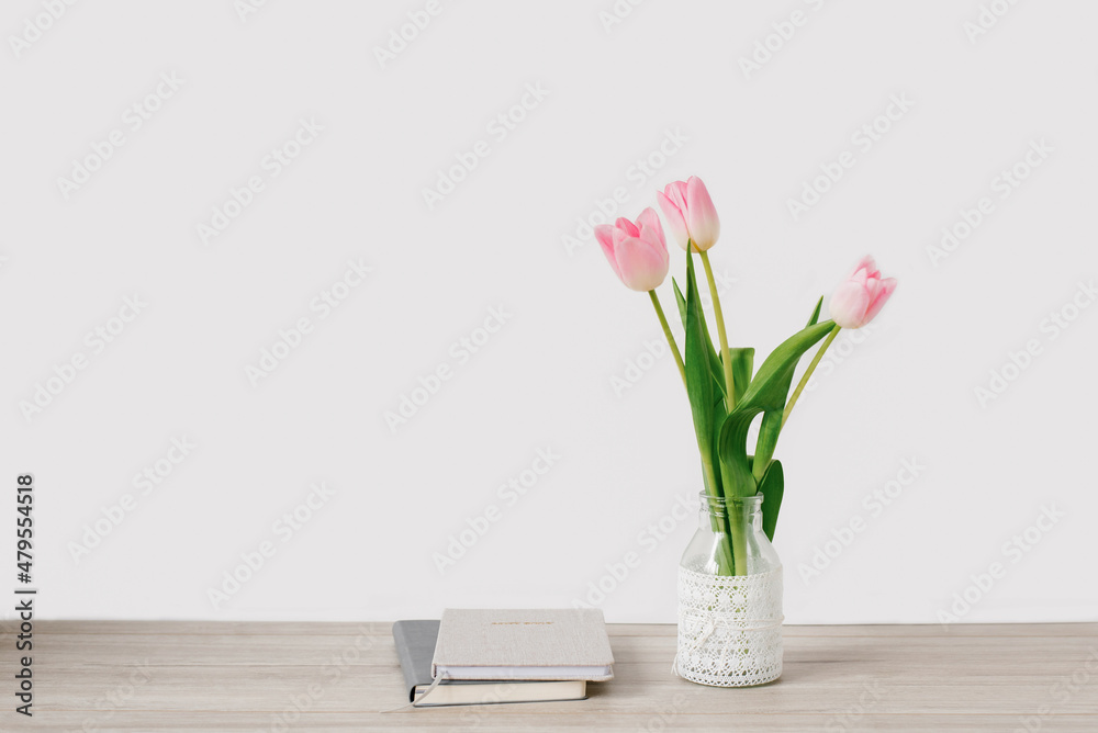 A bouquet of pink tulips of spring flowers in a vase stands on the desktop near the notebooks. Copy space A bouquet of pink tulips of spring flowers in a vase stands on the desktop near the notebooks. Copy space