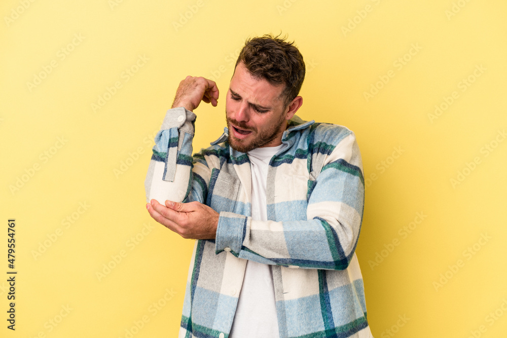 Young caucasian man isolated on yellow background massaging elbow, suffering after a bad movement. Young caucasian man isolated on yellow background massaging elbow, suffering after a bad movement.