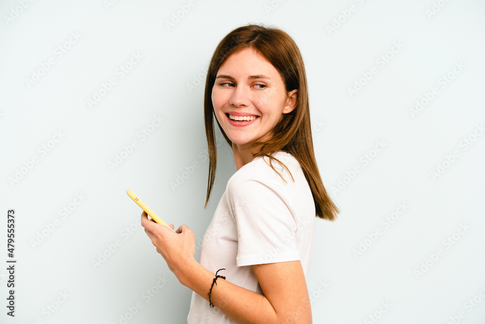 Young English woman holding mobile phone isolated on blue background looks aside smiling, cheerful and pleasant. Young English woman holding mobile phone isolated on blue background looks aside smiling, cheerful and pleasant.