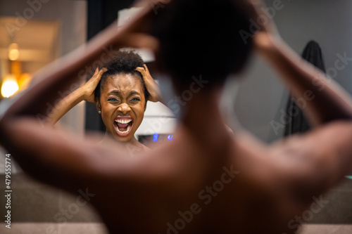 back of young african american woman adjusting hair in mirror and shouting