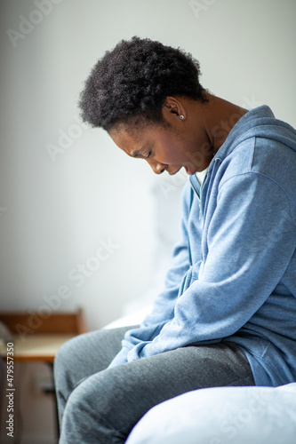 young African American woman siting on side of bed and yawning © mimagephotos