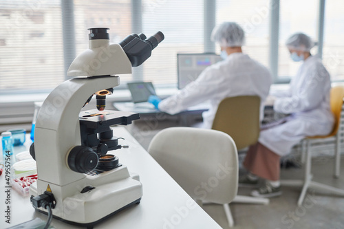 Close-up of microscope on the table in the laboratory with two scientists in the background