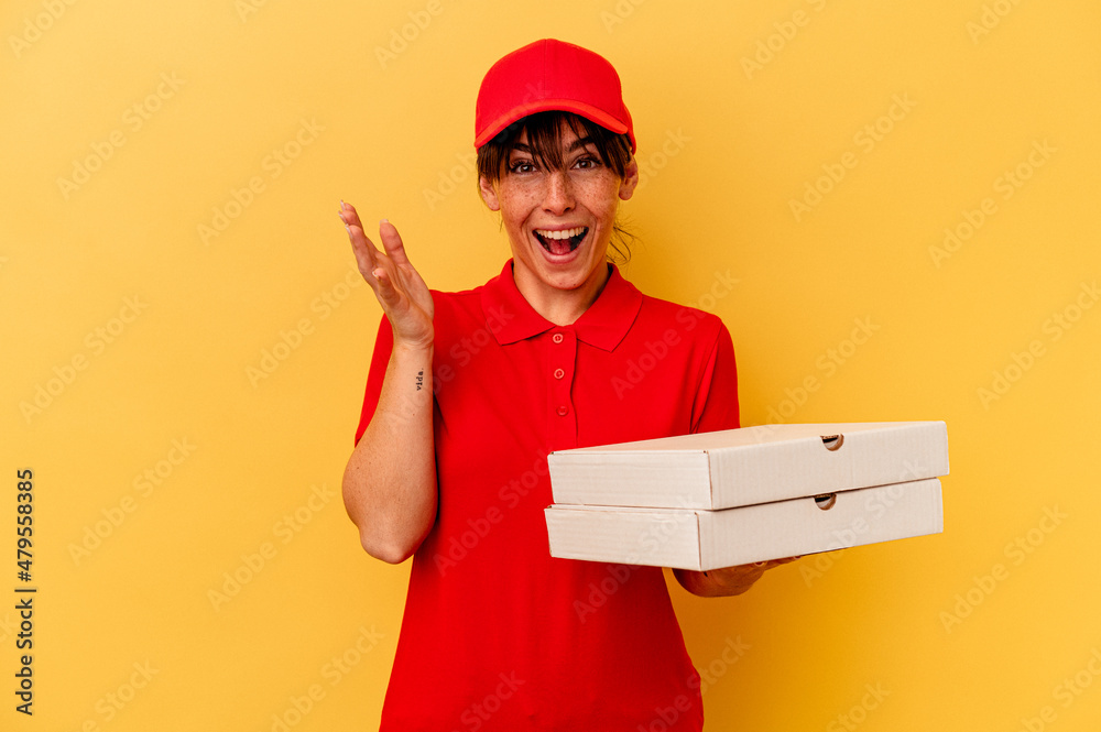 Young delivery woman holding pizzas isolated on yellow background receiving a pleasant surprise, excited and raising hands. Young delivery woman holding pizzas isolated on yellow background receiving a pleasant surprise, excited and raising hands.