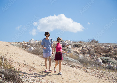 couple in love, teenagers - girl and a guy cheerfully walk along the sandy road on a summer sunny day of vacation. Youth, relaxation, joy, adventure