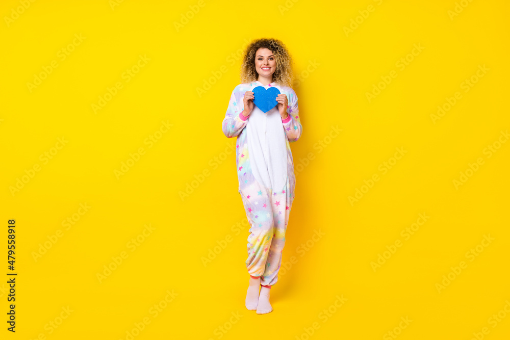 Full length body size view of attractive cheery girl in pajama holding blue form heart isolated on bright yellow color background Full length body size view of attractive cheery girl in pajama holding blue form heart isolated on bright yellow color background