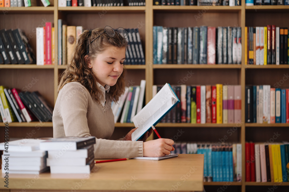 Attractive happy young girl student studying at the college library, sitting at the desk Attractive happy young girl student studying at the college library, sitting at the desk