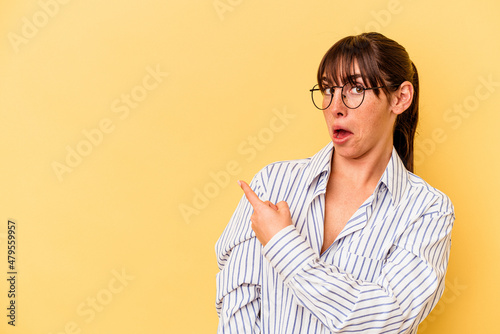 Young Argentinian woman isolated on yellow background smiling and pointing aside, showing something at blank space.