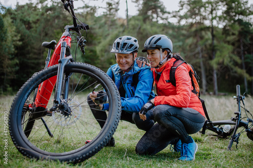 Active senior couple mending bicycle outdoors in forest in autumn day. photo