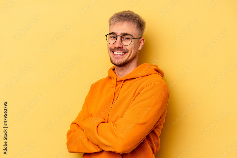 Young caucasian man isolated on yellow background who feels confident, crossing arms with determination. - obrazy, fototapety, plakaty 