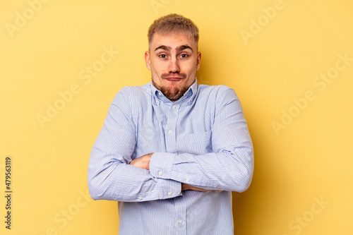 Young caucasian man isolated on yellow background shrugs shoulders and open eyes confused. © Asier