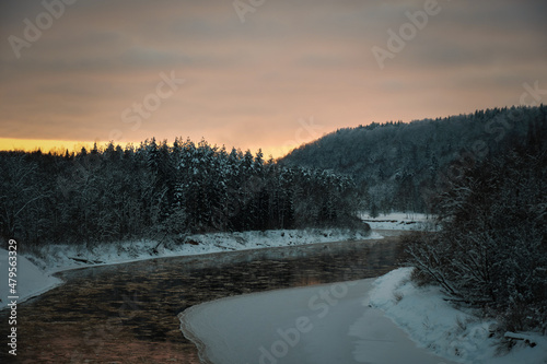 river in winter evening sunset dusk with snowy forest on shores © Martins