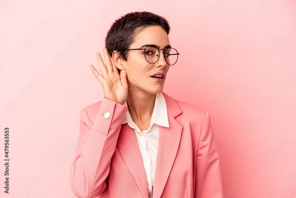 Young business woman wearing a pink blazer isolated on pink background trying to listening a gossip.