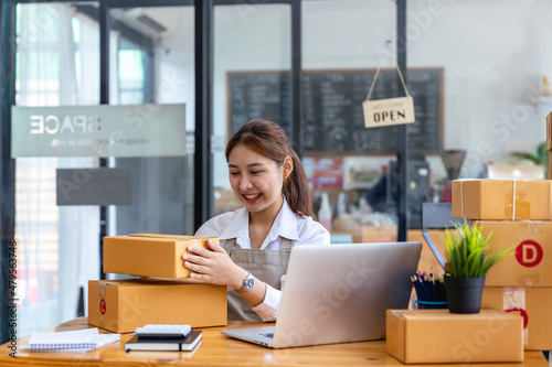 Start up small business entrepreneur SME or freelance asian woman using laptop with box, Young success Asian woman with her hand lift up , online marketing packaging box and delivery, SME concept.